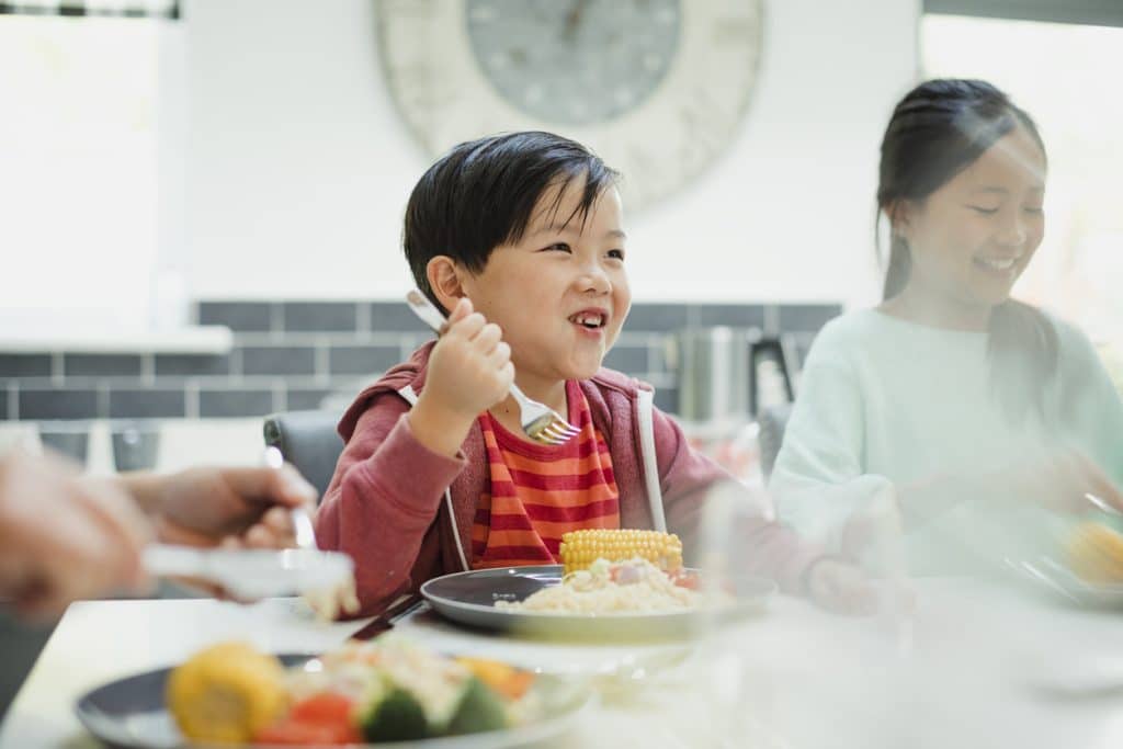 Little boy is enjoying his stir fry dinner and socialising with his family at home.