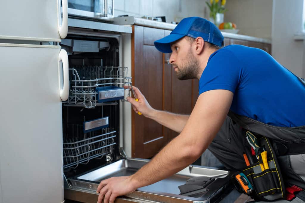 Repairman repairing dishwasher in kitchen.